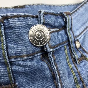 Phần nút cài hình tròn to. Ở giữa có logo của hãng đi kèm chữ True Religion xung quanh